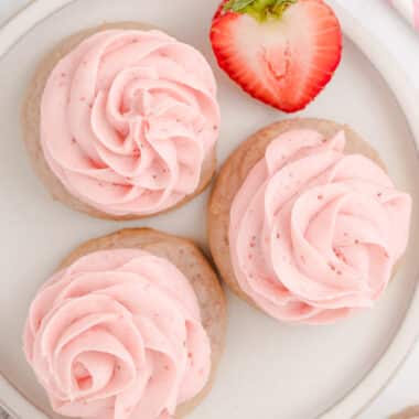 three frosted strawberry cookies on a plate