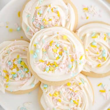 soft and buttery sugar cookies with frosting and sprinkles on a plate