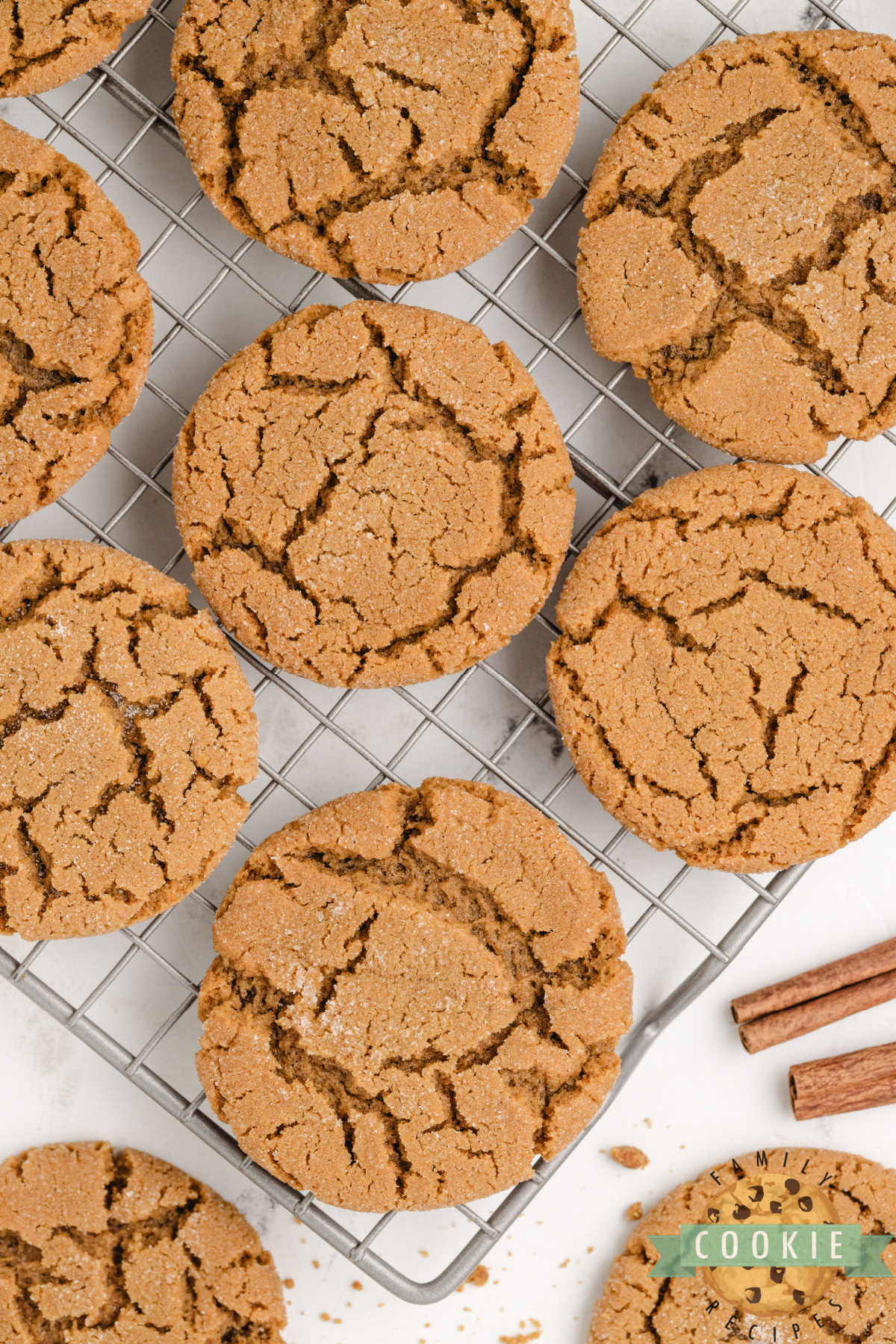 Freshly baked gingerbread cookies cooling on a wire rack with festive ribbon and cinnamon sticks nearby.