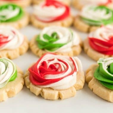 Frosted Rose Sugar Cookies are buttery, soft sugar cookies with a delicious swirled rosette on top! This sugar cookie recipe doesn’t require any chilling and you don’t have to roll them out either! Elegant Sugar Cookies that look like roses that are perfect as gifts!