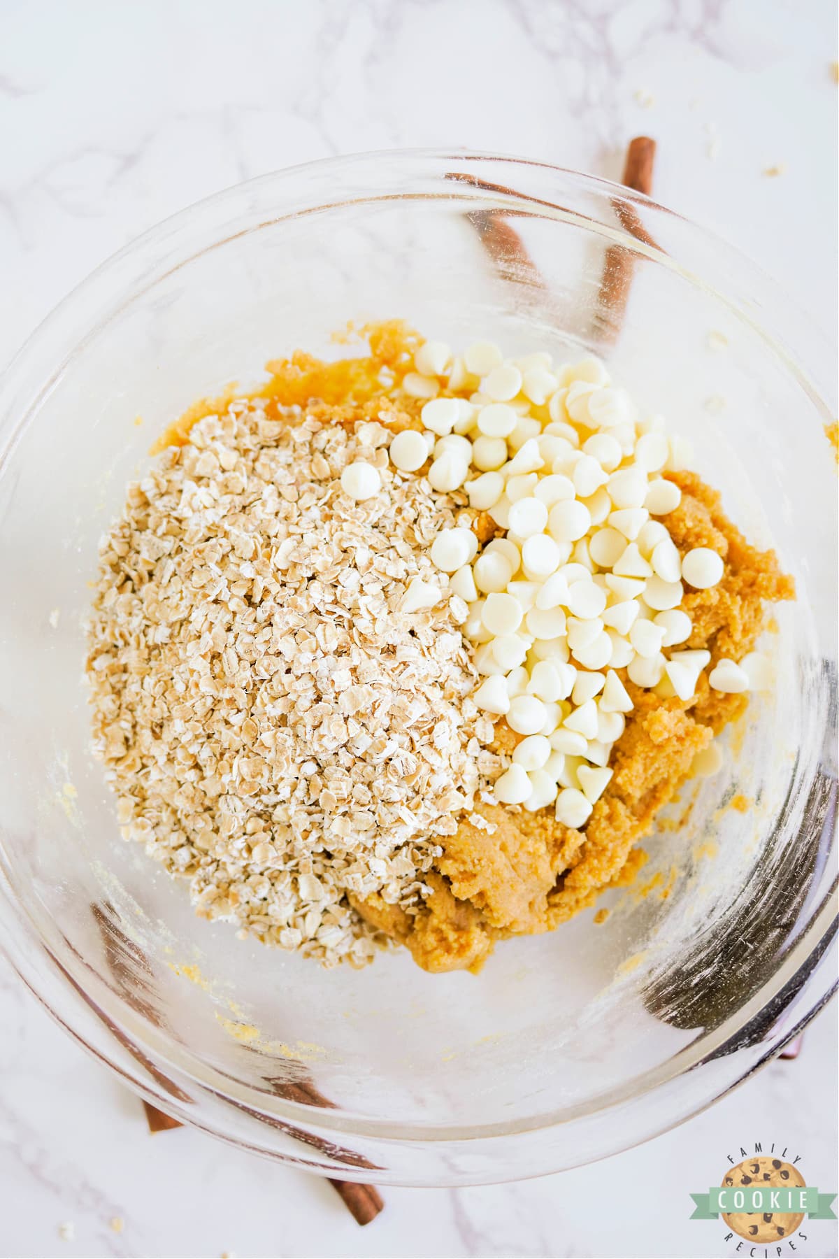 Adding oats and white chocolate chips to pumpkin cookie dough.