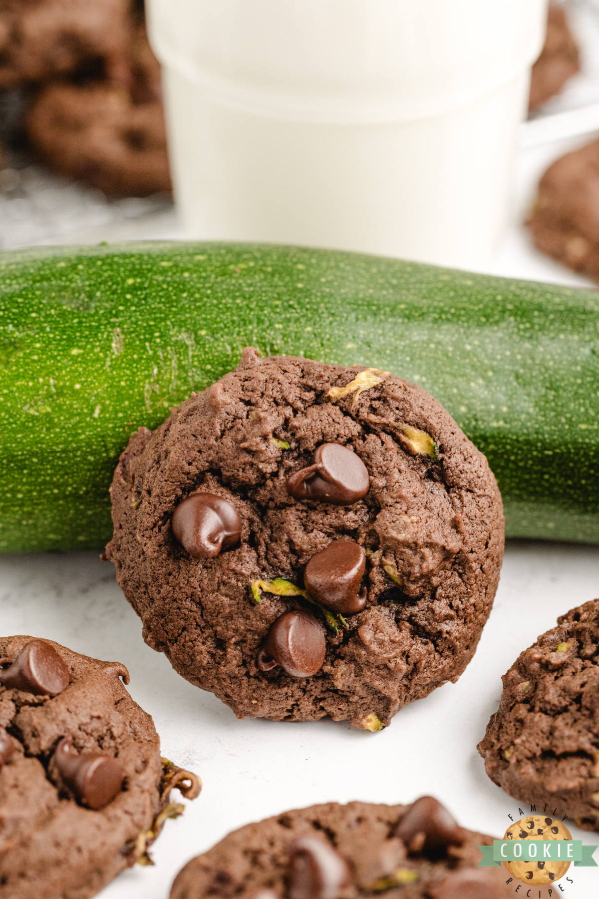 One large chocolate zucchini cookie in front of a large zucchini.