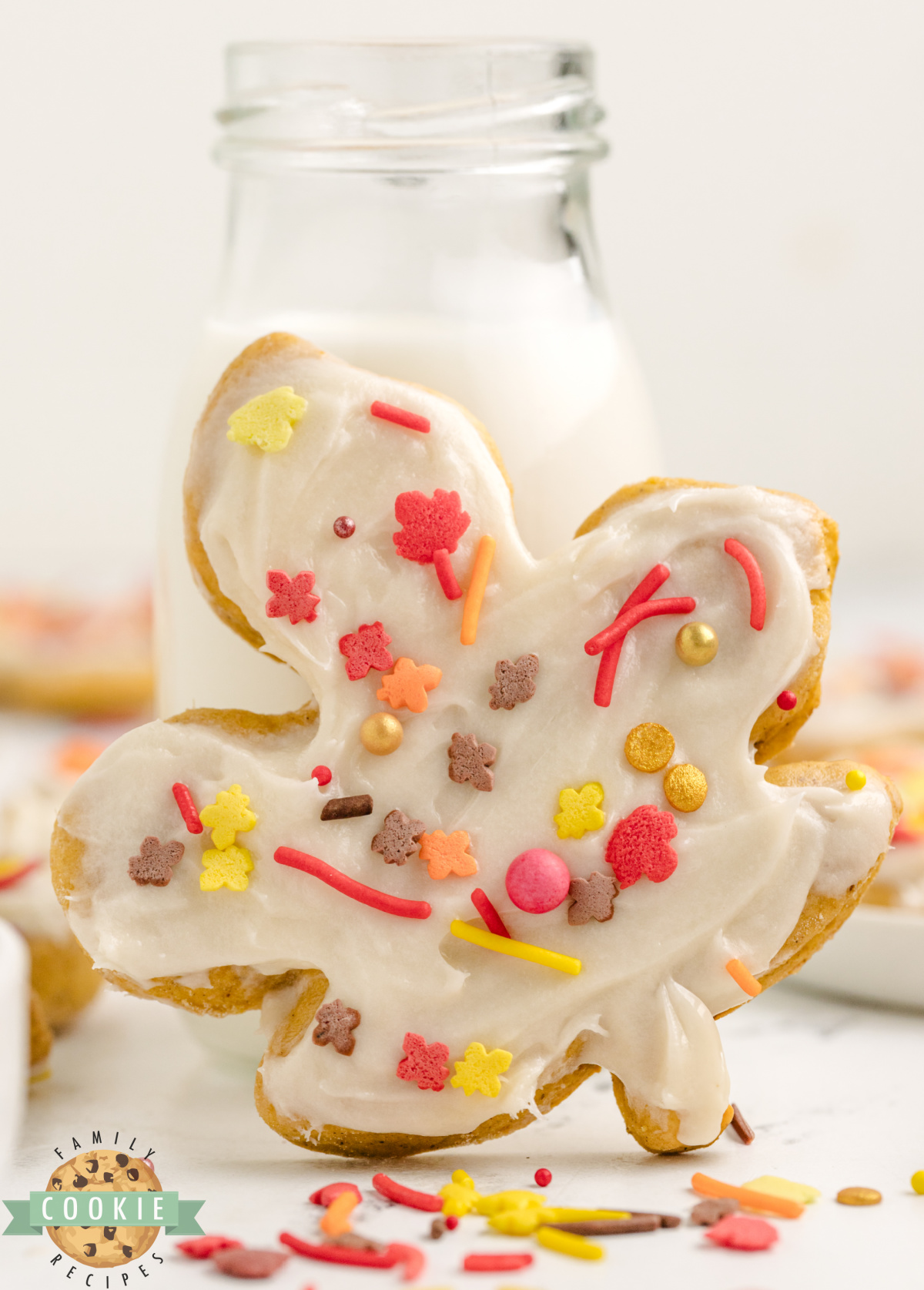 A decorated Pumpkin Sugar Cookie with a glass of milk.
