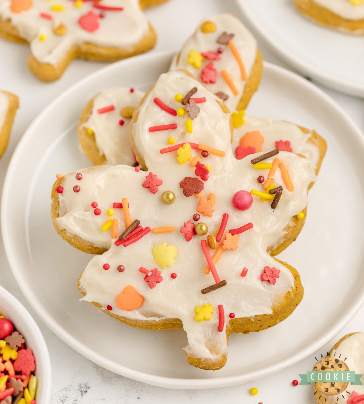 Close-up of frosted Pumpkin Sugar Cookies with cream cheese frosting and sprinkles.