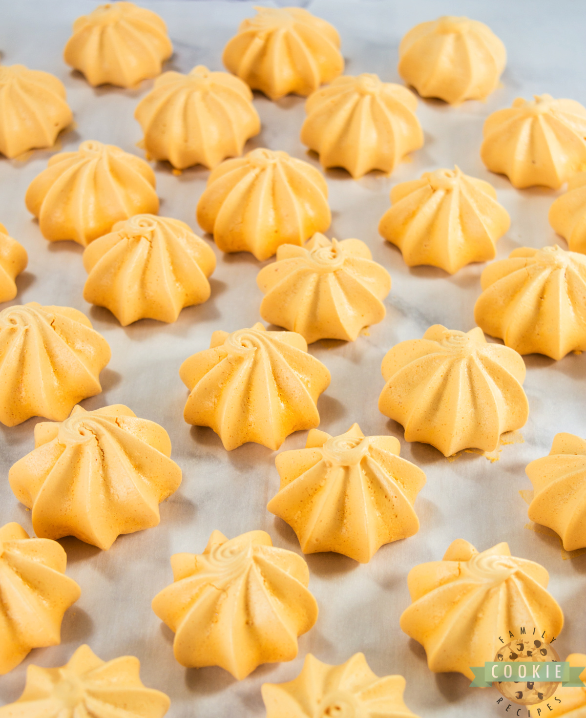 Tray of bright orange Pumpkin Meringues cooling on parchment paper.