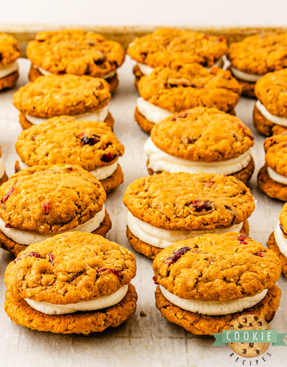 Pumpkin cranberry sandwich cookies with cream cheese filling arranged neatly on parchment paper.