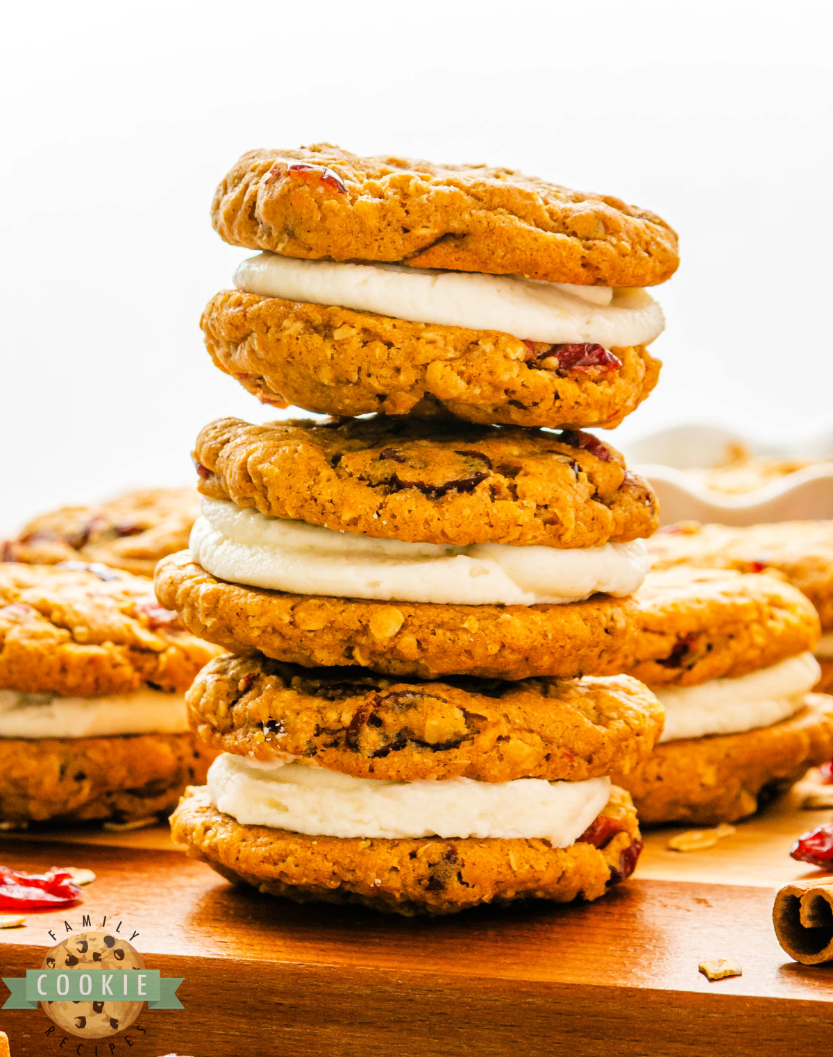 Soft pumpkin oatmeal cookies with dried cranberries and creamy frosting filling stacked on a plate.