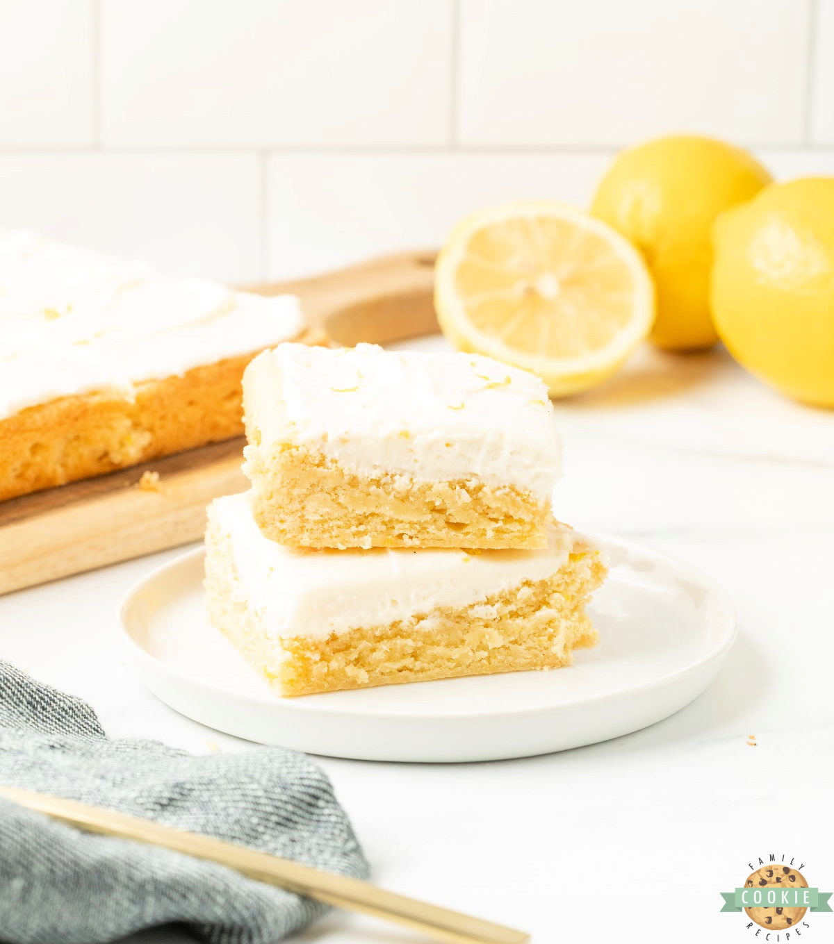 Lemon cookie bars cut into squares and topped with cream cheese frosting and fresh lemon zest on a white plate.

