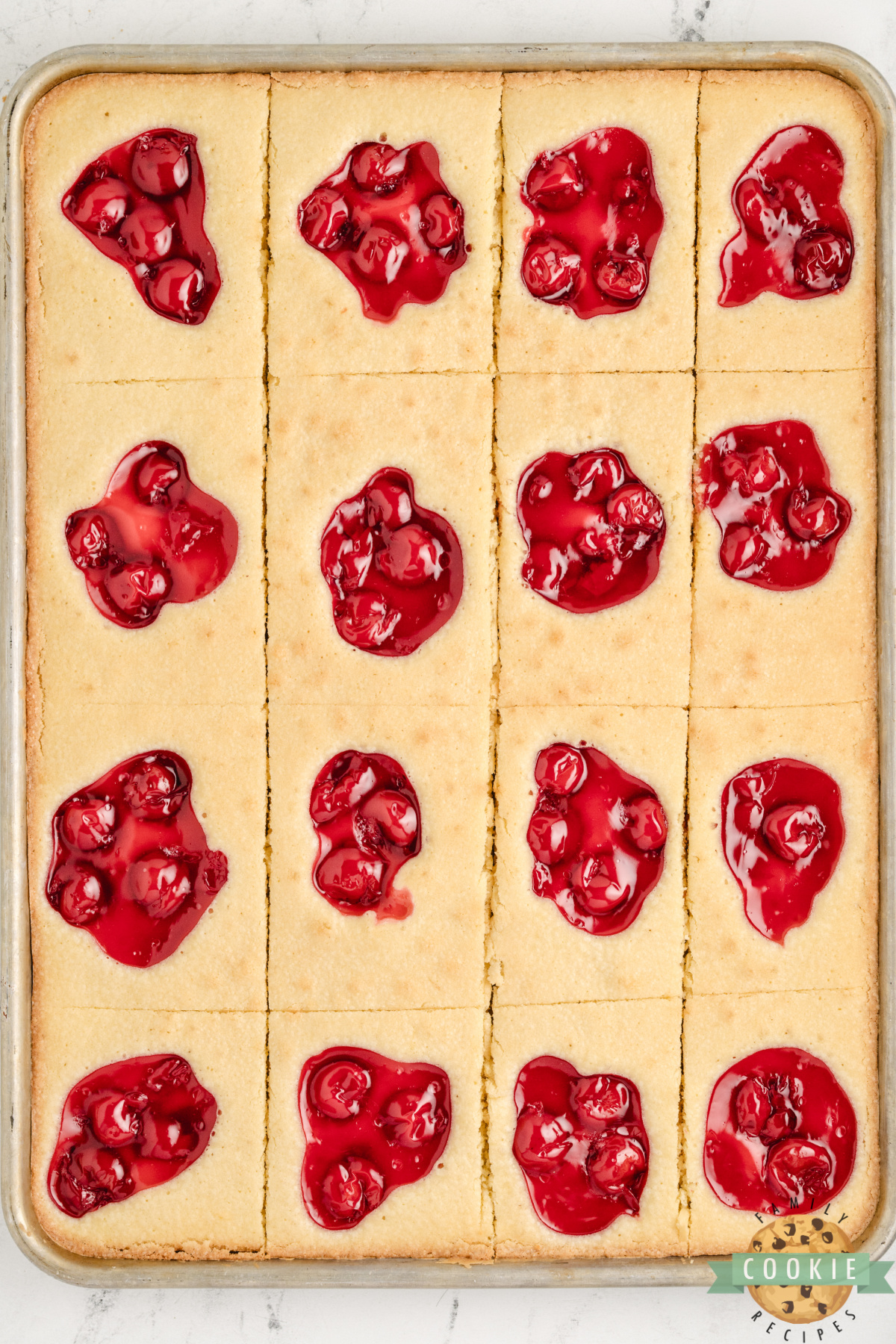 Overhead view of cherry pie cookie bars on a baking sheet cut into squares with cherry topping.